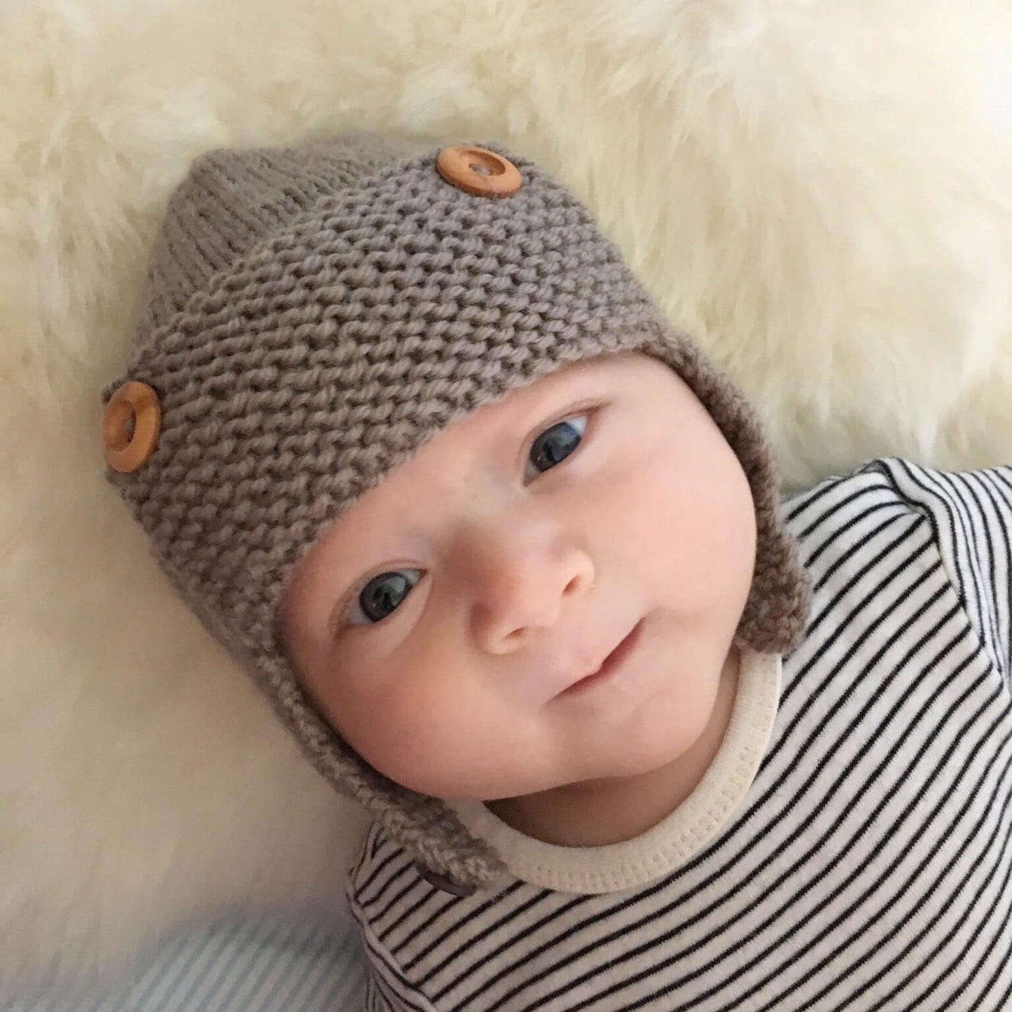 a baby aviator knitting pattern show modelled on a baby laying on a fluffy blanket