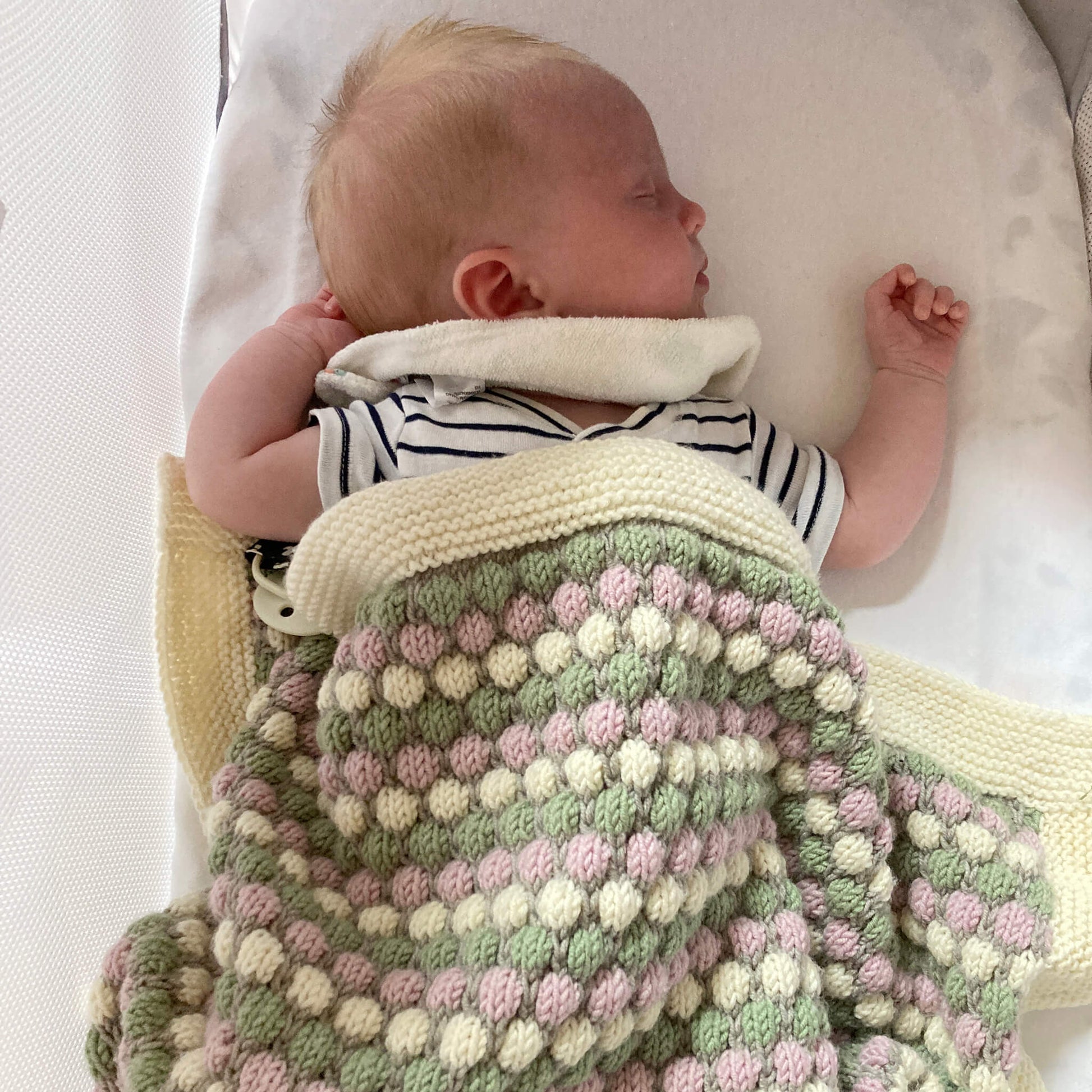 a sleeping baby modelling a baby blanket knitting pattern in use