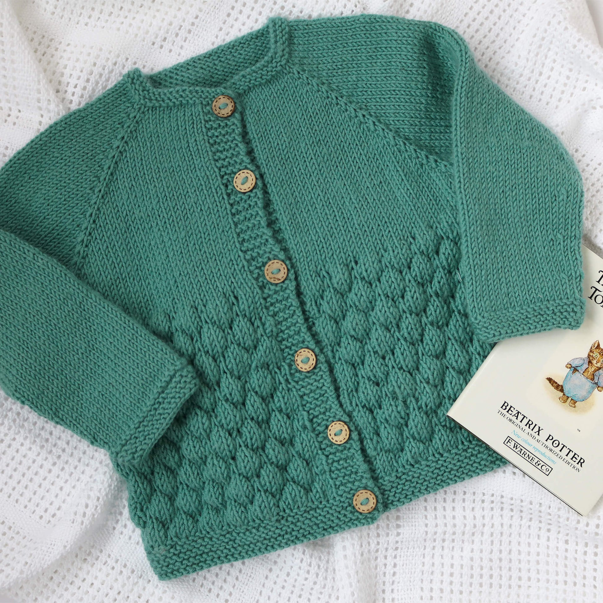 a sample for a baby cardigan knitting pattern the cardigan is knit from the top down and shown in turquoise colour yarn