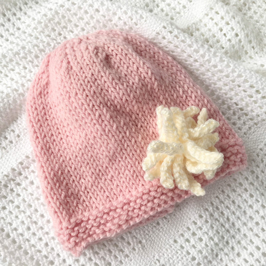 a baby and child hat knitting pattern with flower. shown knitted in pink with cream flower