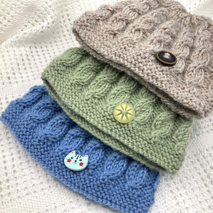 a baby hat knitting pattern with cables. three colour versions are shown, green, blue and light brown