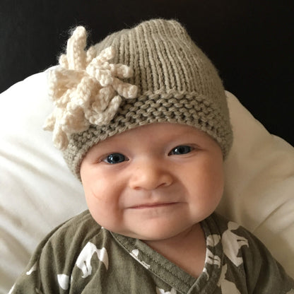 a smiling baby modelling a baby hat pattern with flower