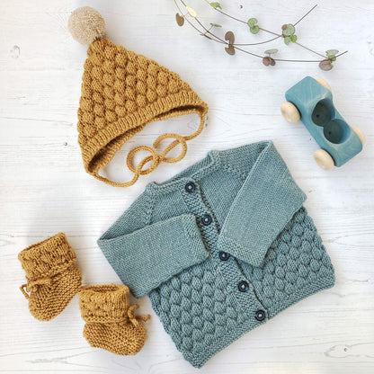 a baby outfit knitting pattern which includes a cardigan, a pixie hat and booties all with a bubble stitch pattern feature