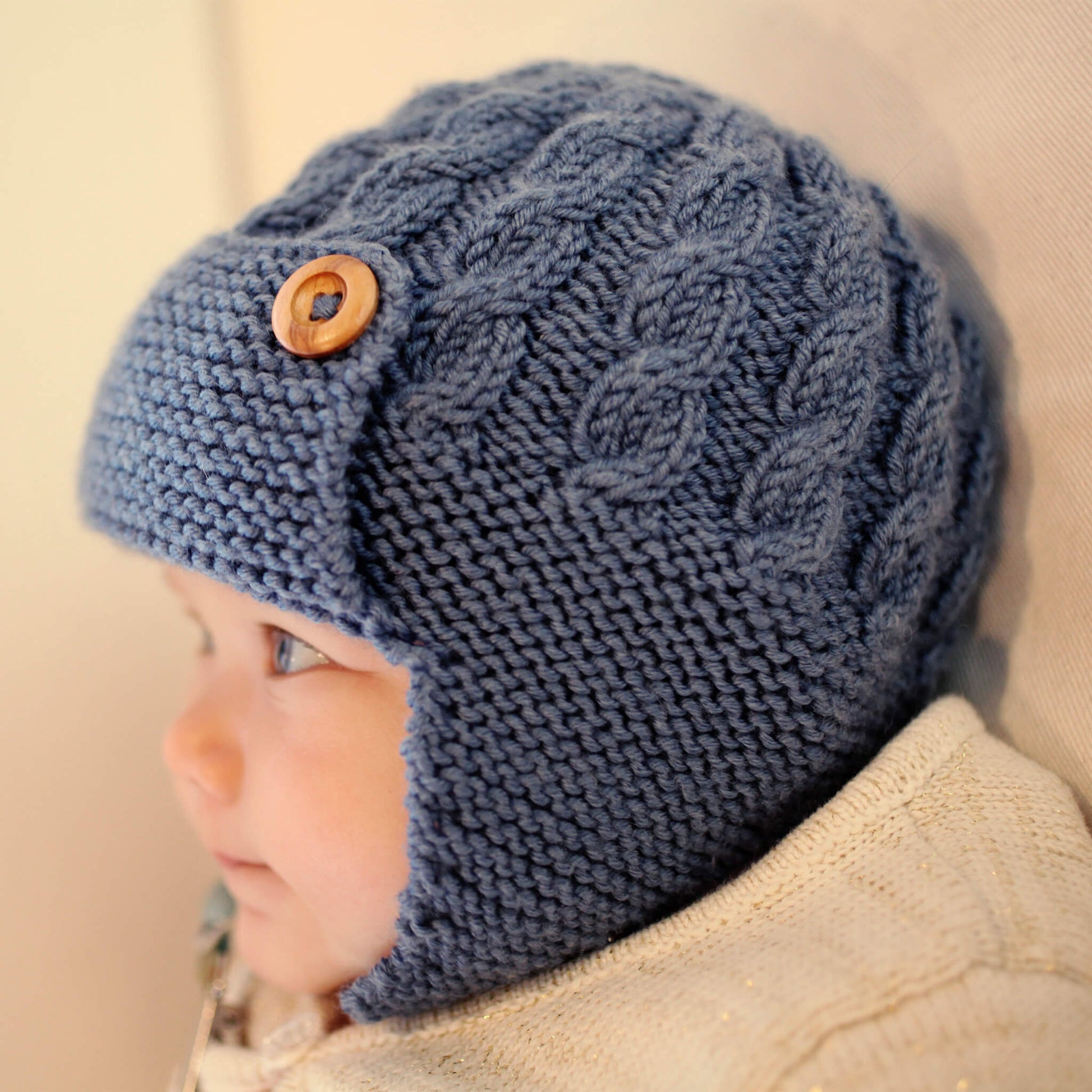 child wearing aviator hat. The aviator hat knitting pattern features a cable design