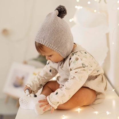 a baby pixie bonnet knitting pattern. baby is sitting amongst lights playing with a toy