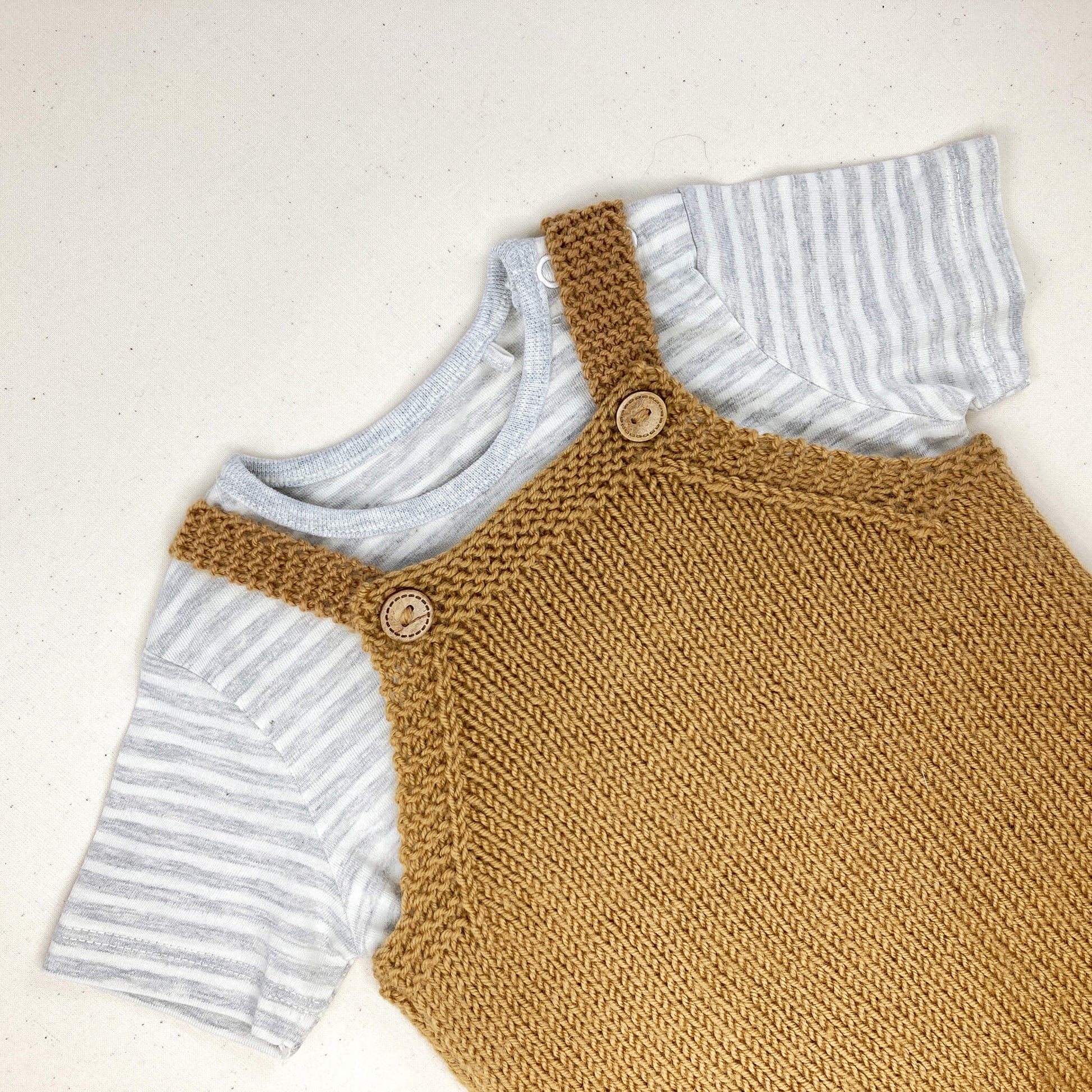 baby all-in-one knitting pattern shown worn over a striped T shirt