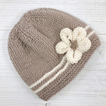 a beginner knitter baby hat pattern . colour is taupe with white stripes and a flower embellishment