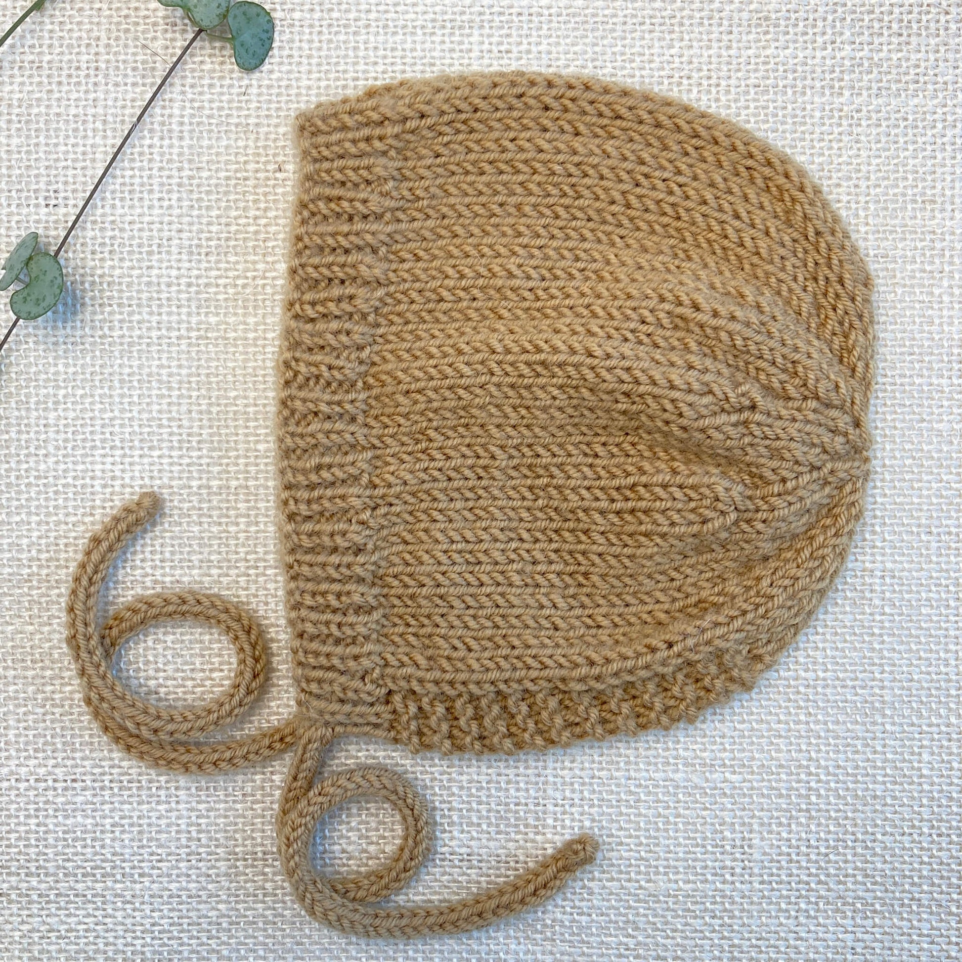 a beginner knitting pattern for a baby bonnet shown in mustard colour yarn