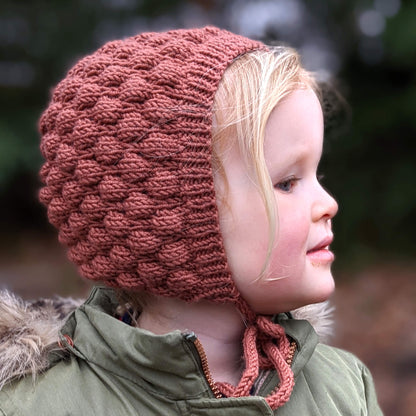 Child wearing bonnet knit using bubble stitch bonnet knitting pattern