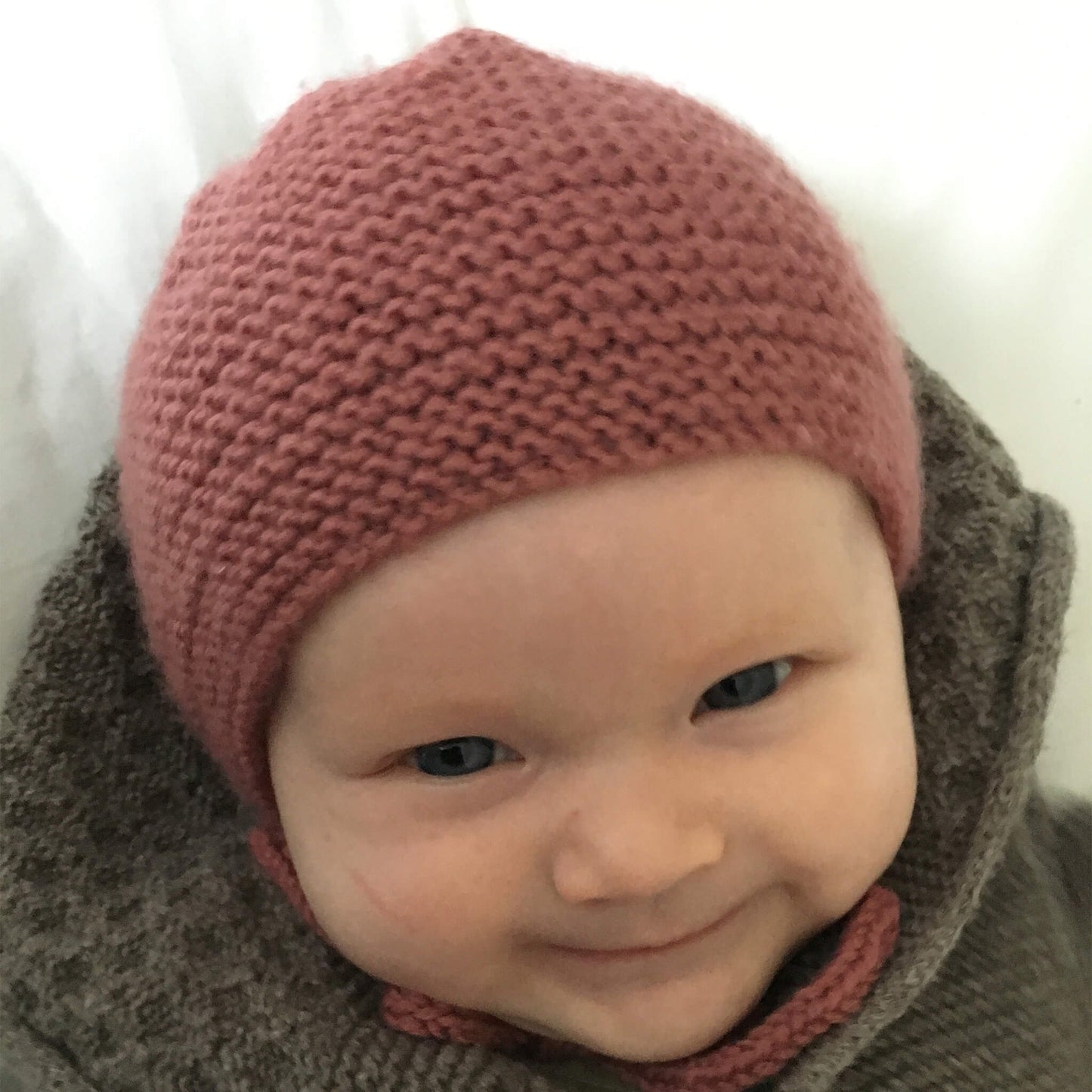 smiling baby modelling a hat for a bonnet knitting pattern