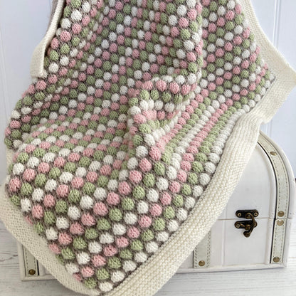 bubble stitch baby blanket knitting pattern. the blanket is draped over a toy chest