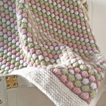 a bubble stitch blanket knit pattern. blanket sample draped over a storage chest