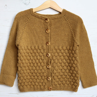 a sample for a bubble stitch knitting pattern for a baby cardigan . the cardigan is knit in mustard colour yarn and photographed on a hanger