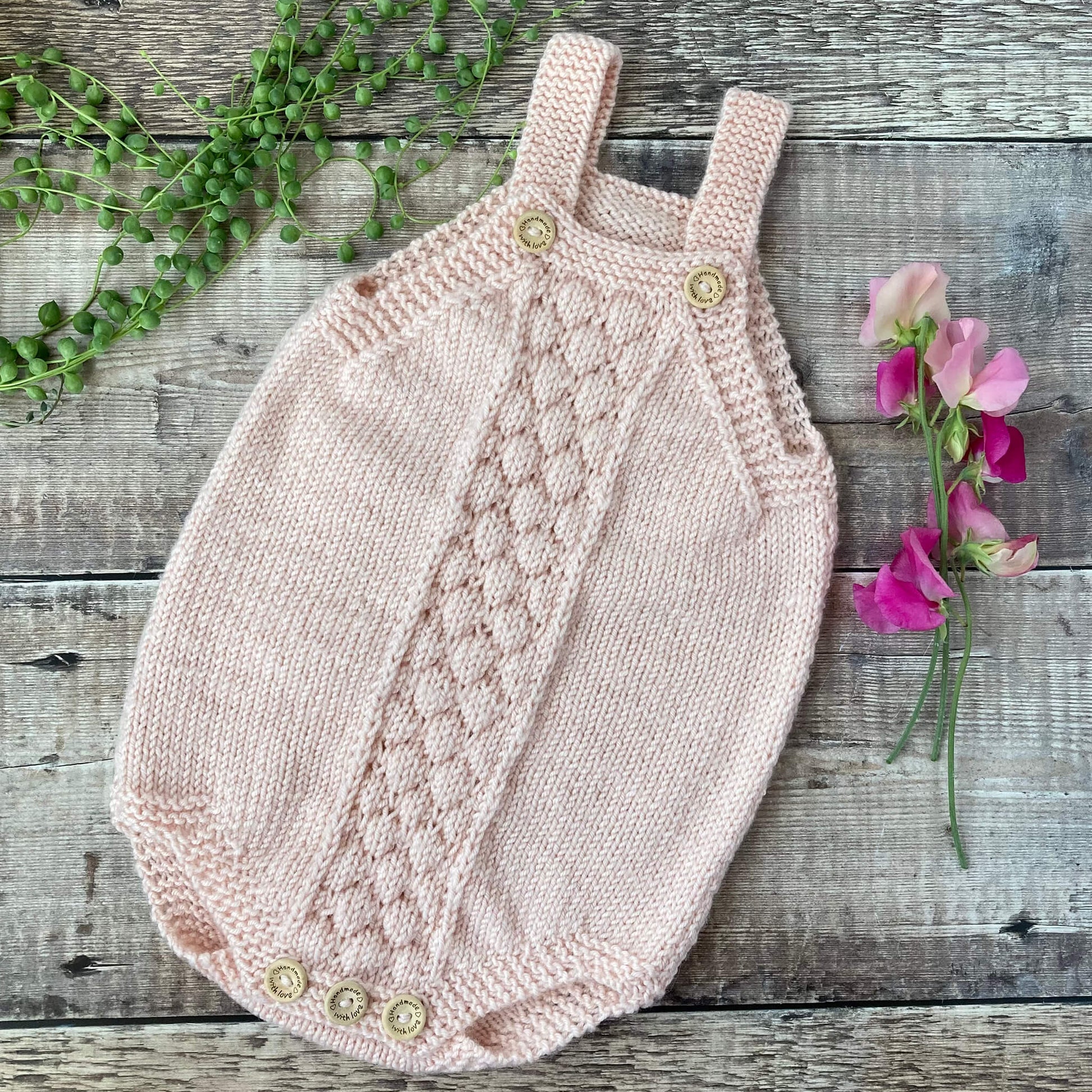 bubble stitch romper knitting pattern sample in pink yarn on hardwood floor