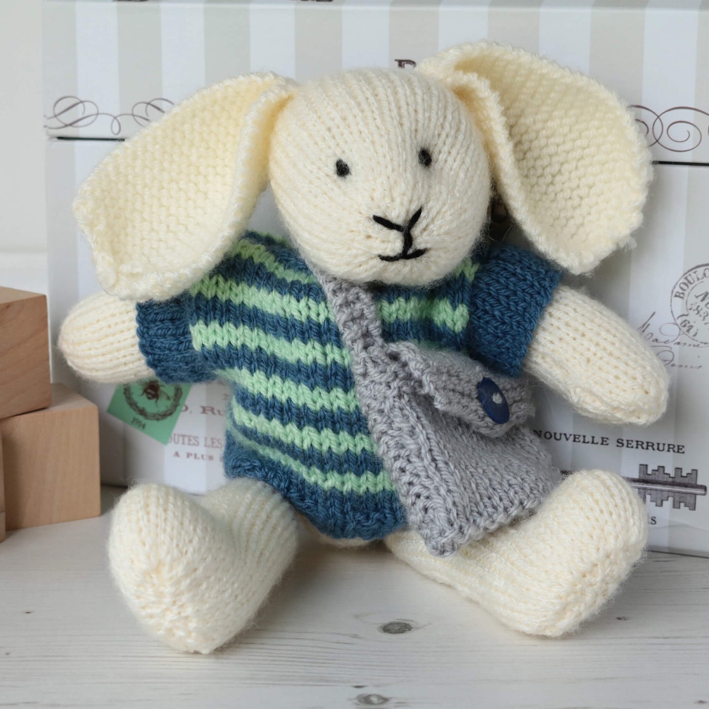 a bunny doll knitting pattern. the bunny is sitting against a toy chest