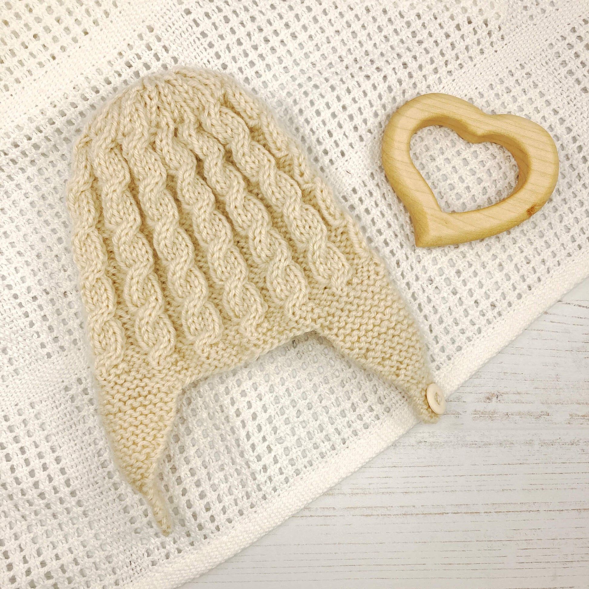 a cable knit hat pattern for a baby shown knitted in cream colour yarn