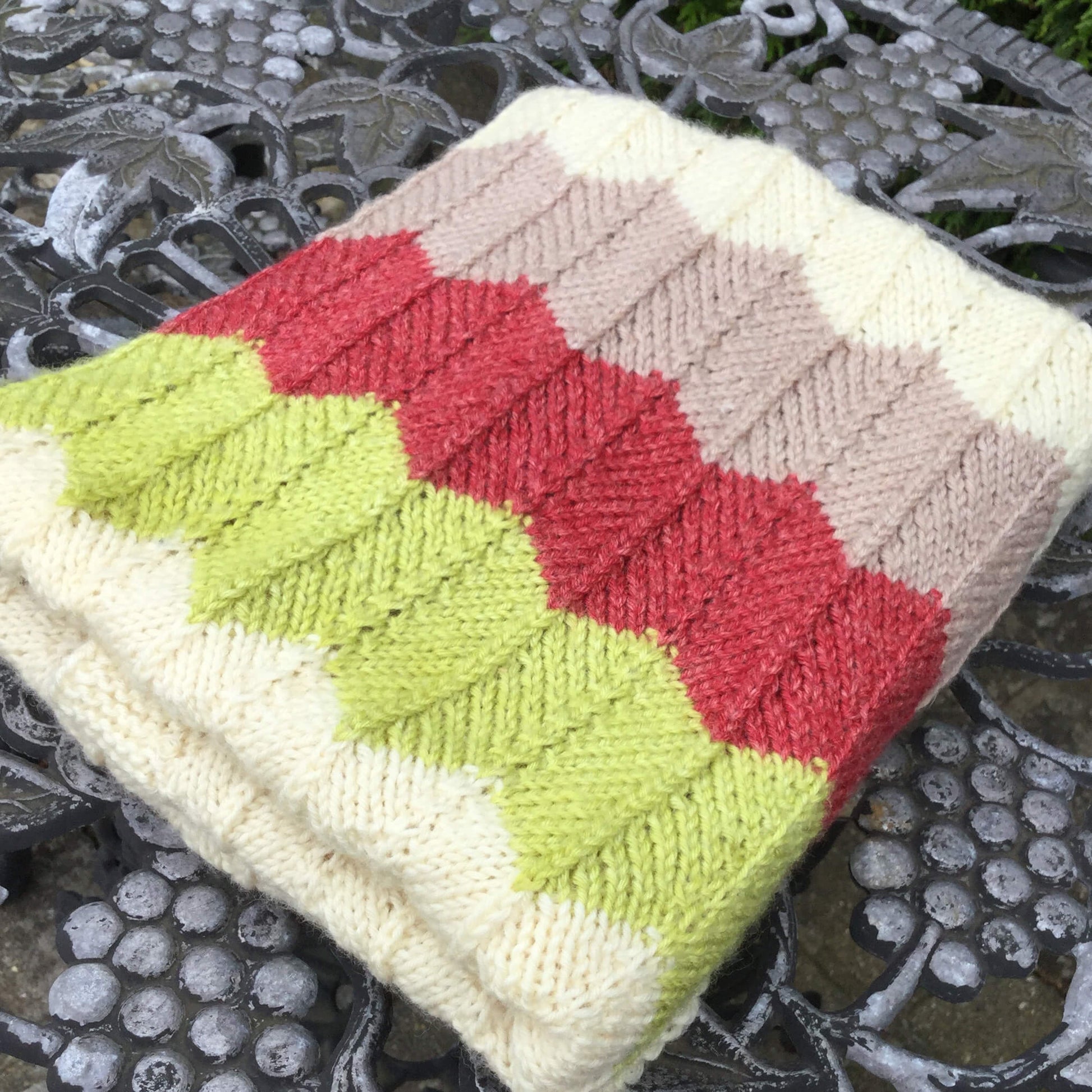 a chevron baby blanket knitting pattern shown in red , green and taupe stripes