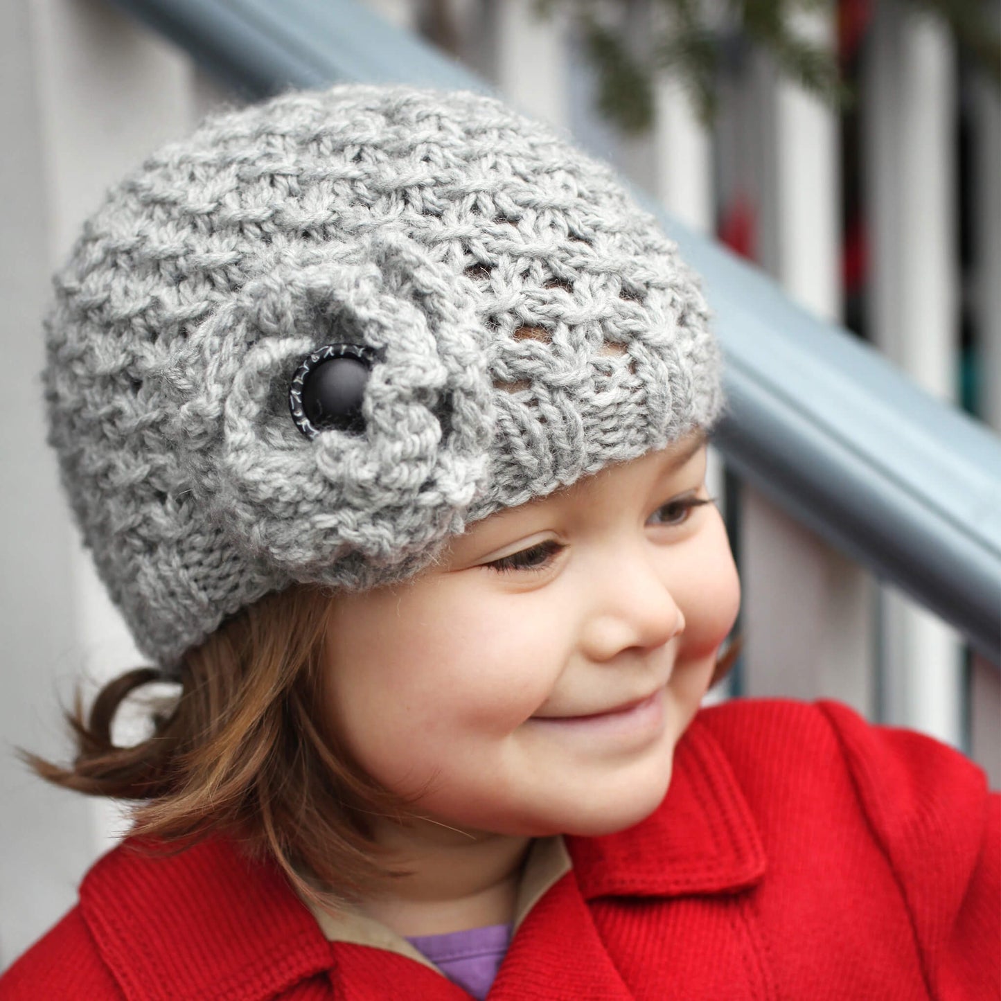 a chunky lace hat knitting pattern with flower modelled by a girl in a red coat