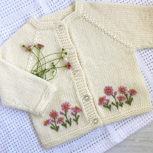 a daisy embroidered baby cardigan knitting pattern laying on a white blanket. 