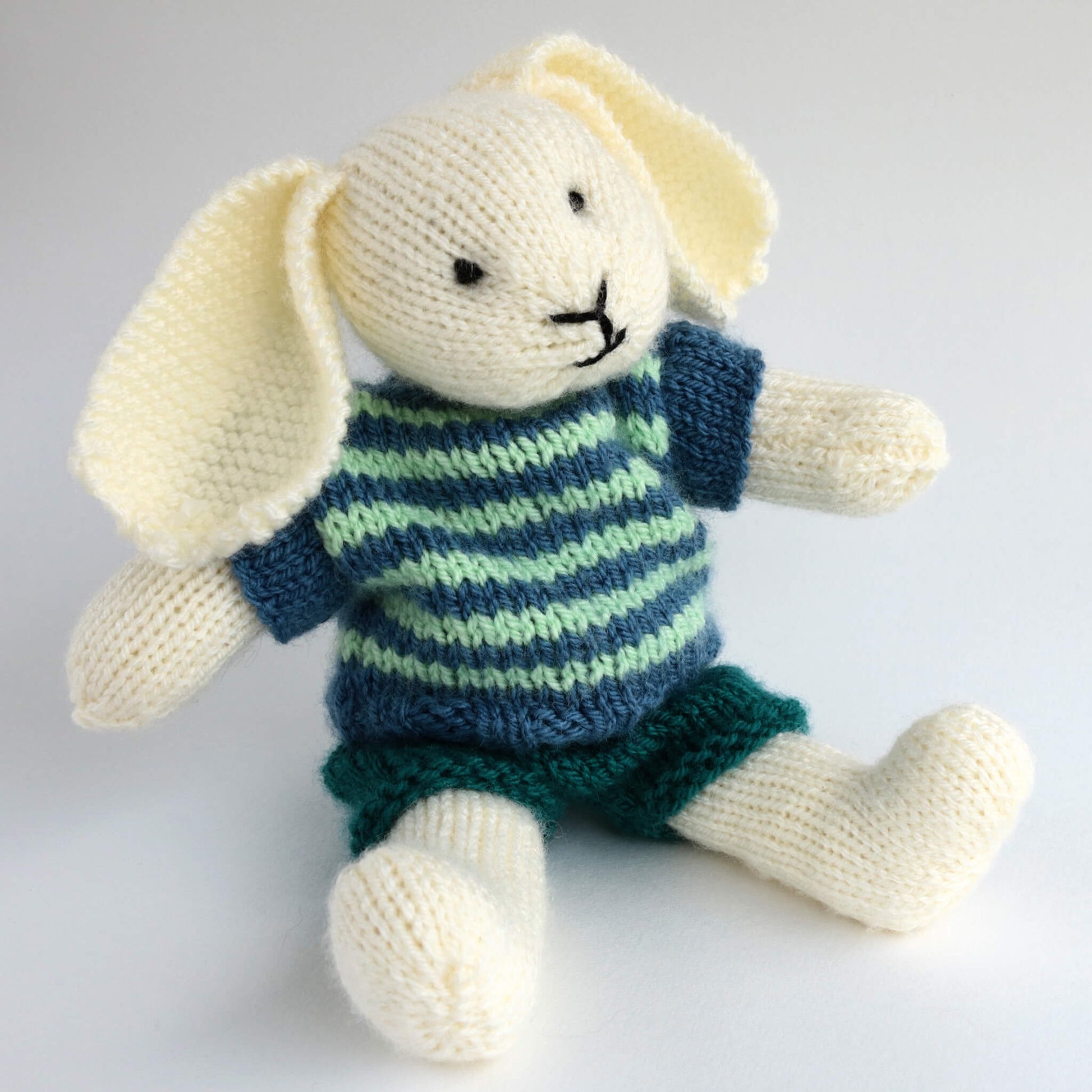 a dressed bunny knitting pattern. bunny shown is sitting wearing shorts and a striped top