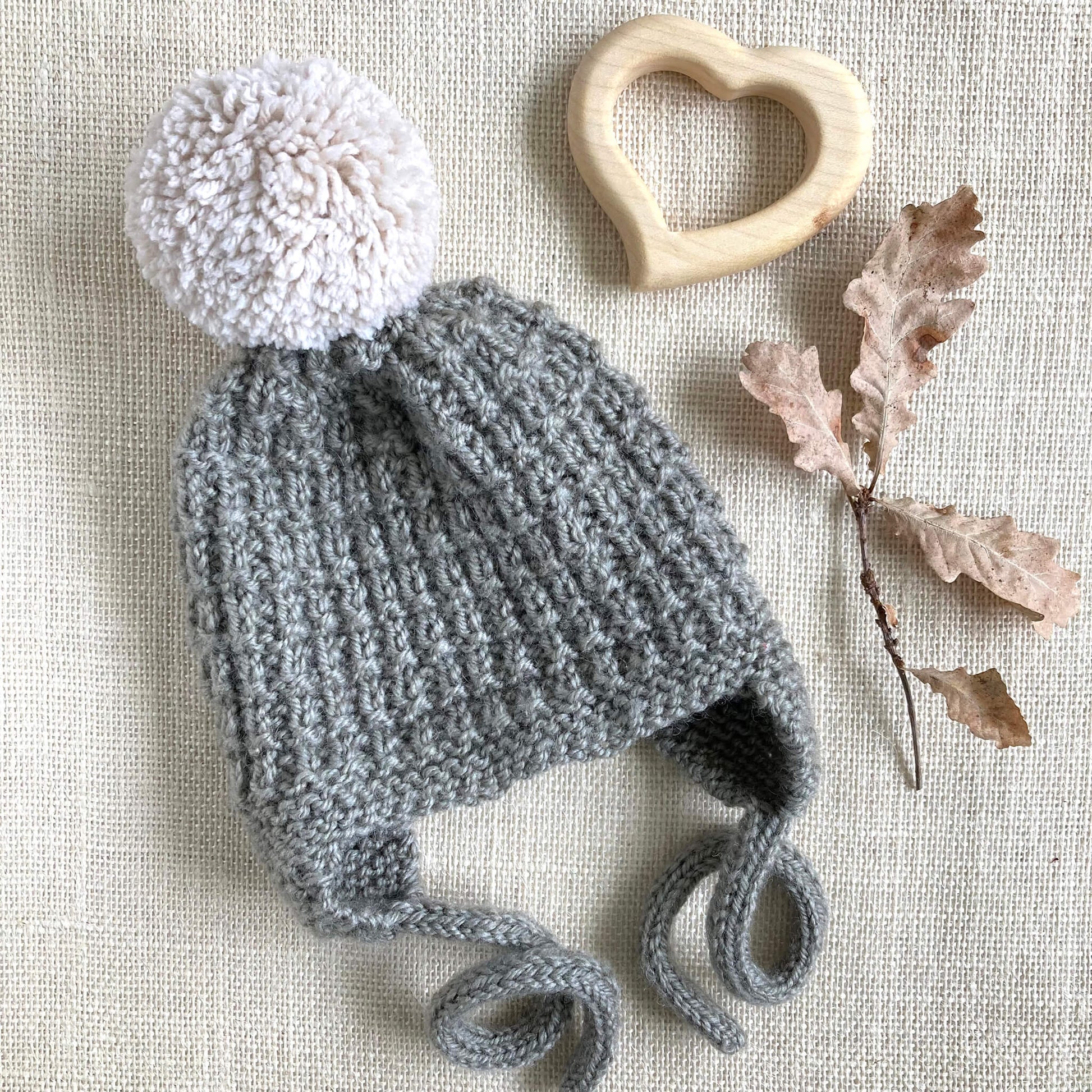 an easy earflap hat knitting pattern . sample is knit in grey yarn with off white pompom