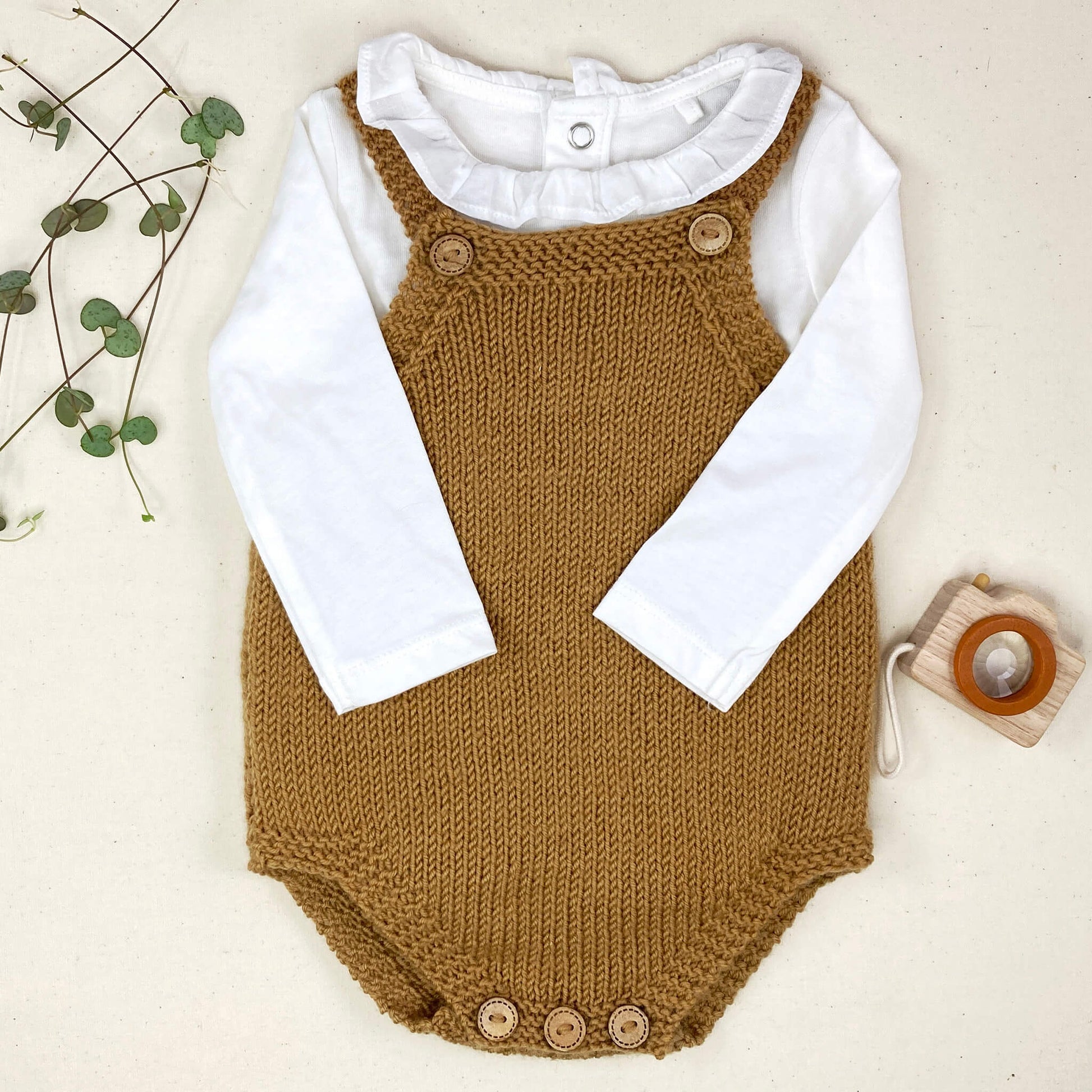 an easy baby romper knitting pattern. the romper is shown styled with a white top with a frilled collar