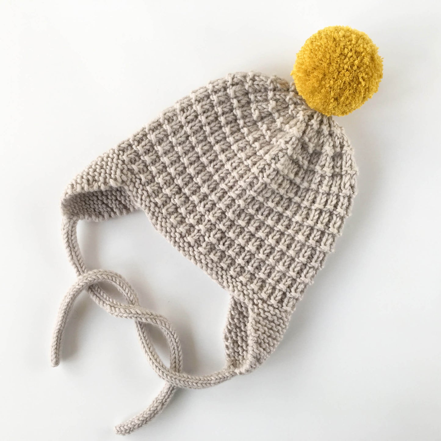 an easy to knit earflap hat pattern form kids shown in grey yarn with yellow pompom