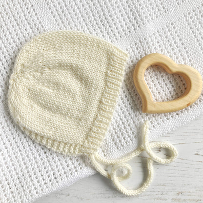 white baby bonnet laying on blanket as sample for an easy knitting pattern