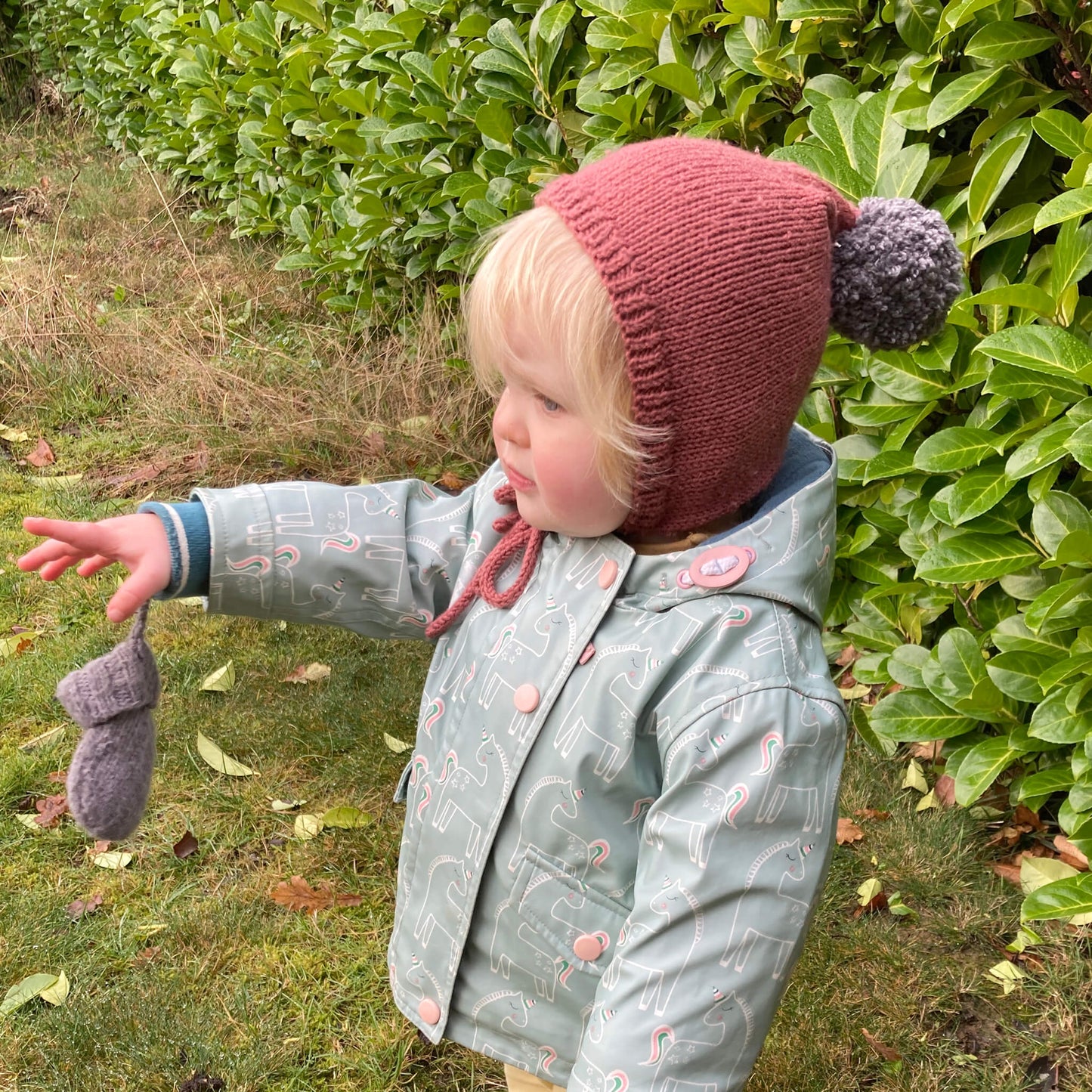 an easy knitting pattern for a bay pixie hat. photo shows a toddler wearing a rust coloured hat pointing