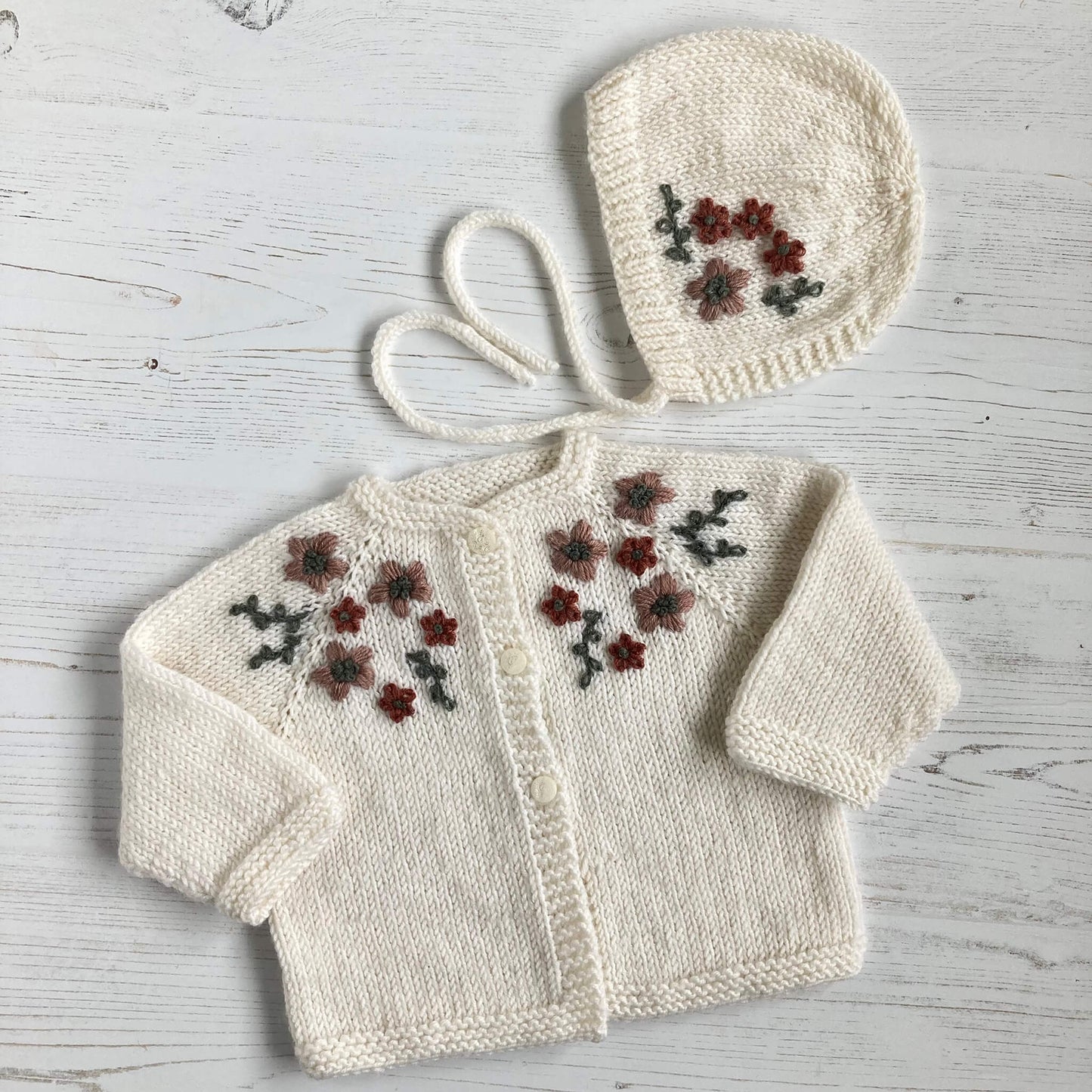 a knitting pattern for embroidered baby clothes. the cardigan and bonnet both have matching flower embroidery