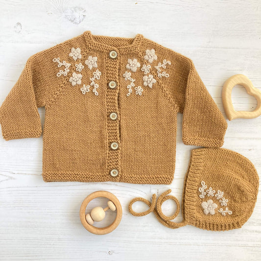 embroidered baby knitting patterns for a cardigan and matching bonnet. Flower embroidery is in white on mustard knitting