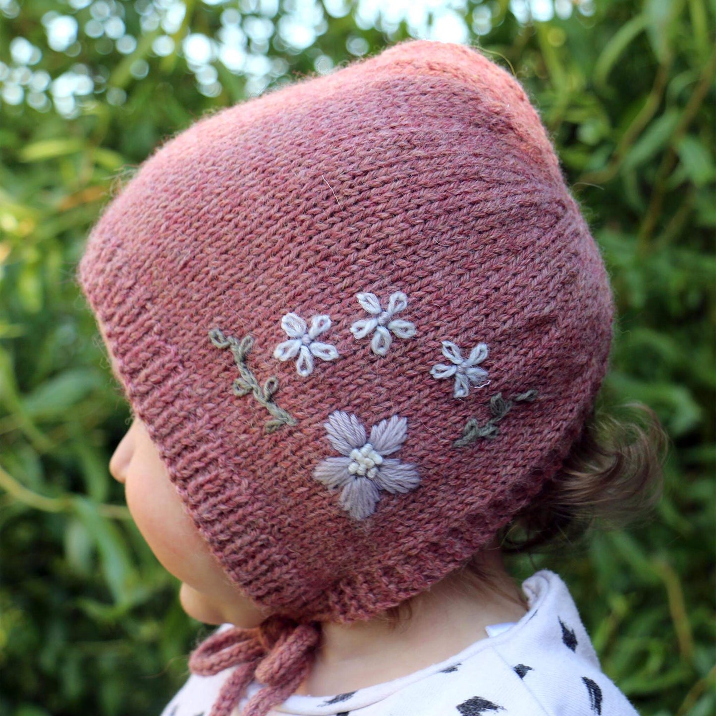 girl wearing bonnet with floral embroidery for knitting pattern