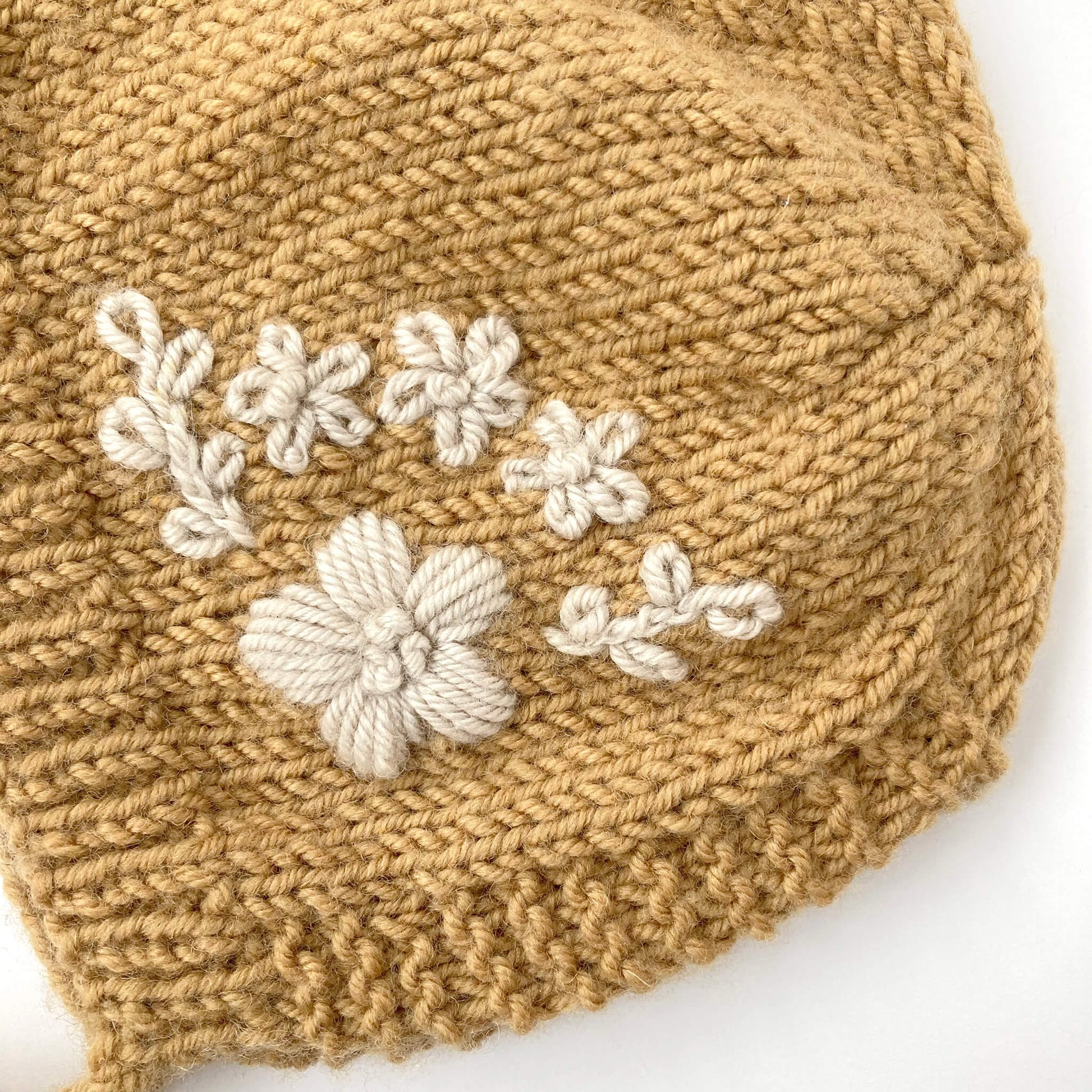 close up photo of embroidery on knitting pattern for baby bonnet