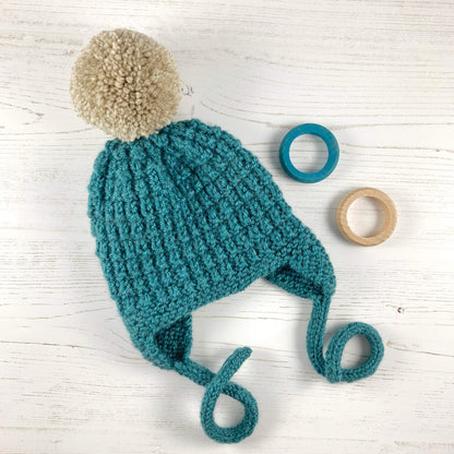 a hat knitting pattern for babies and children. sample shown in turquoise with light grey pompom