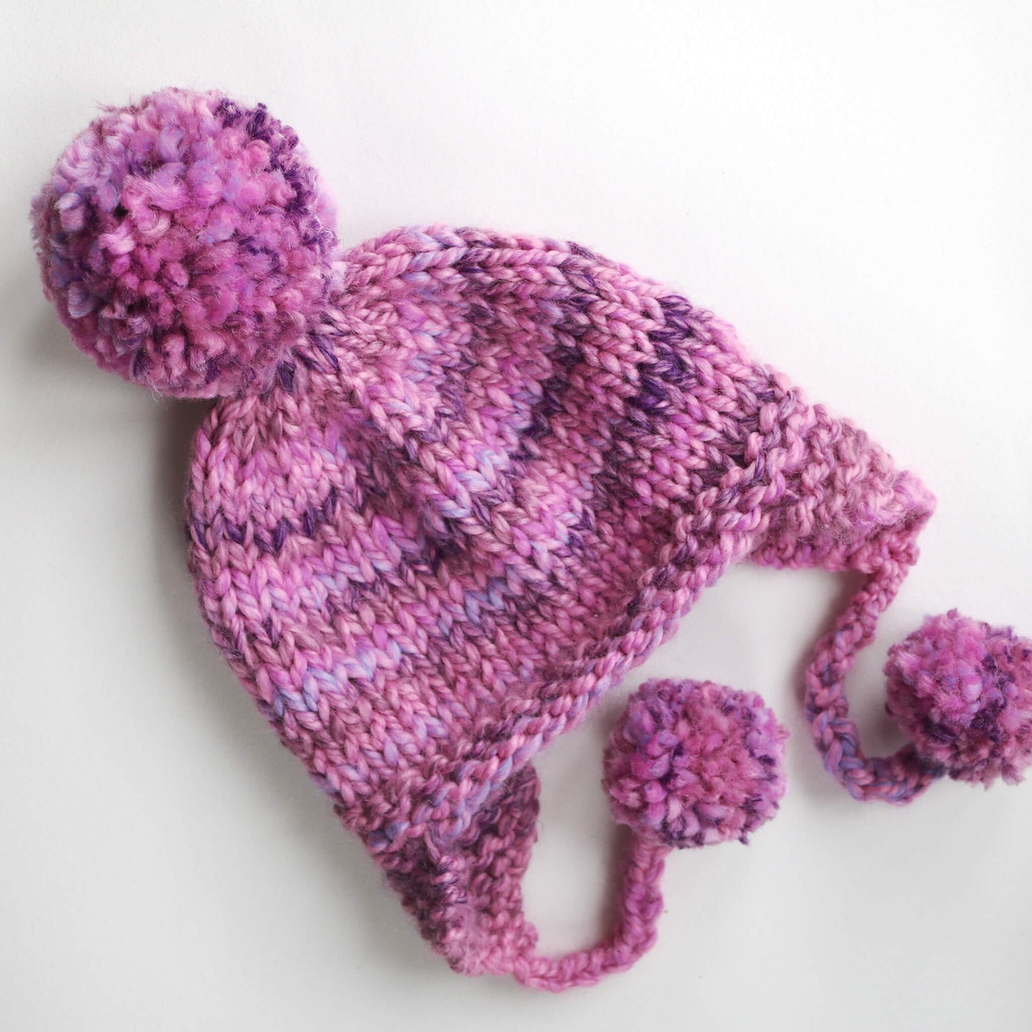 a kids pompom hat pattern shown in variegated pink yarn