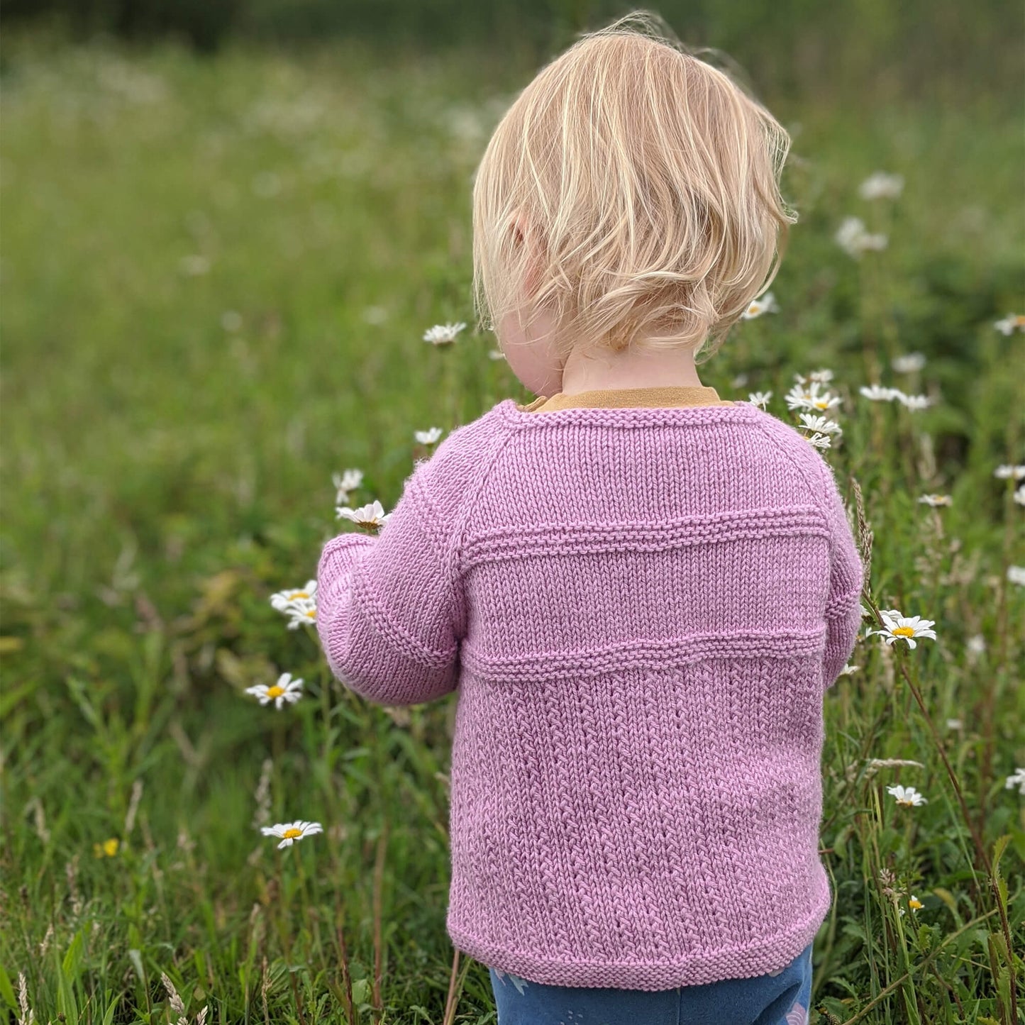 a toddler showing the rear view of a cardigan knitting pattern