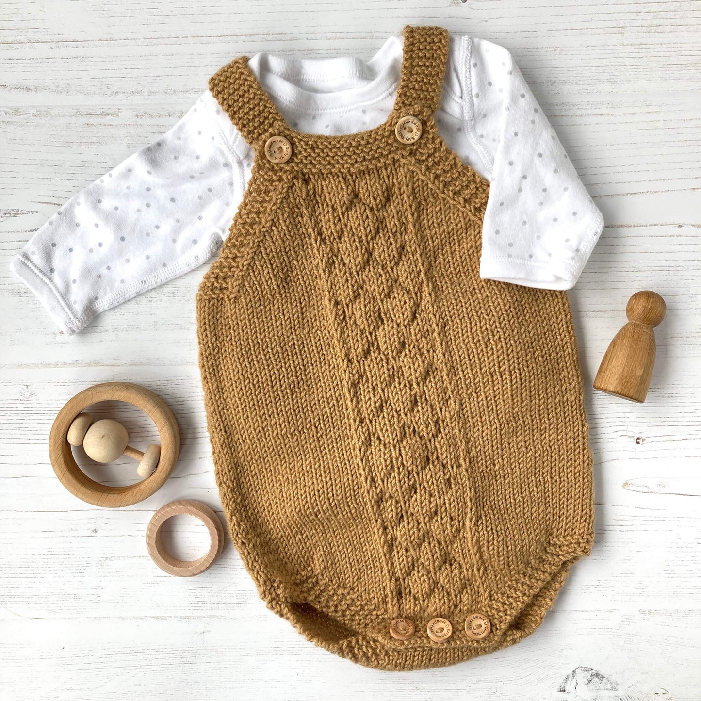 a baby romper knitting pattern sample in mustard yarn styled with a long sleeved onesie