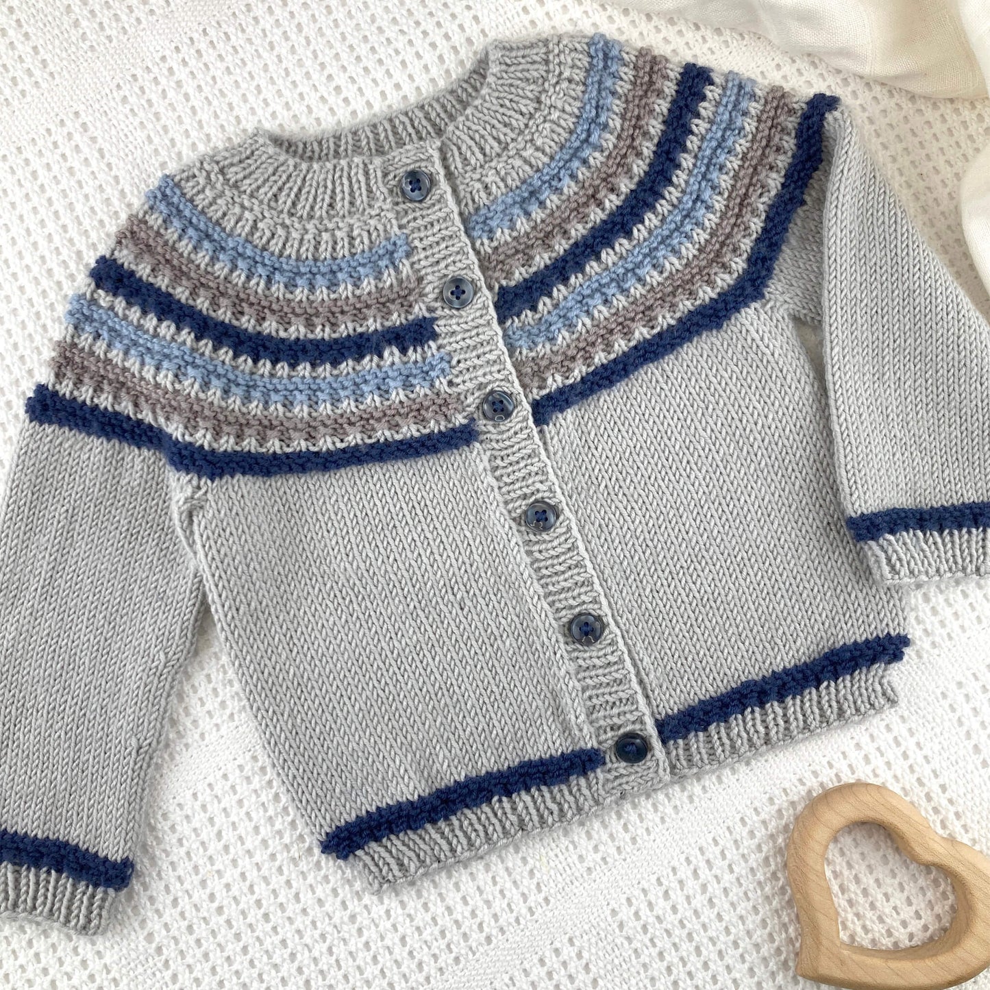 a sample for a knit pattern for a baby cardigan, shown in grey with navy , blue and brown stripes