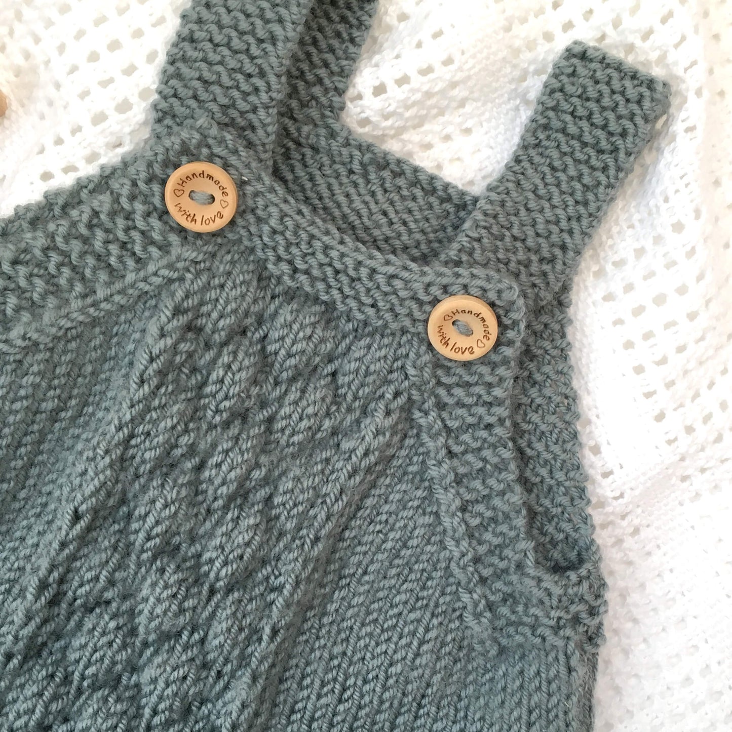 close up of bubble stitch and button fastening straps on baby romper knitting pattern