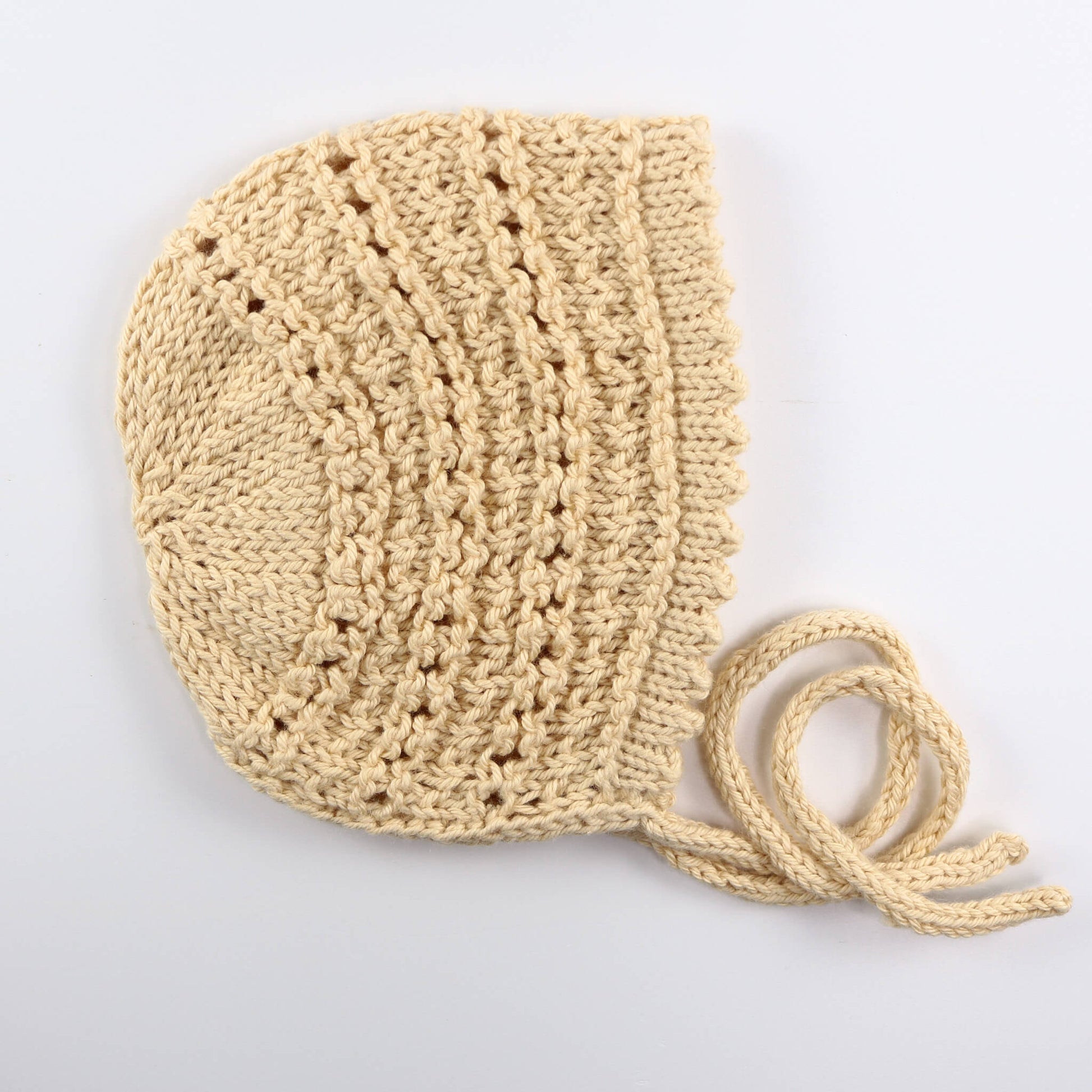 a knit pattern for a lace bonnet shown knitted in cream yarn