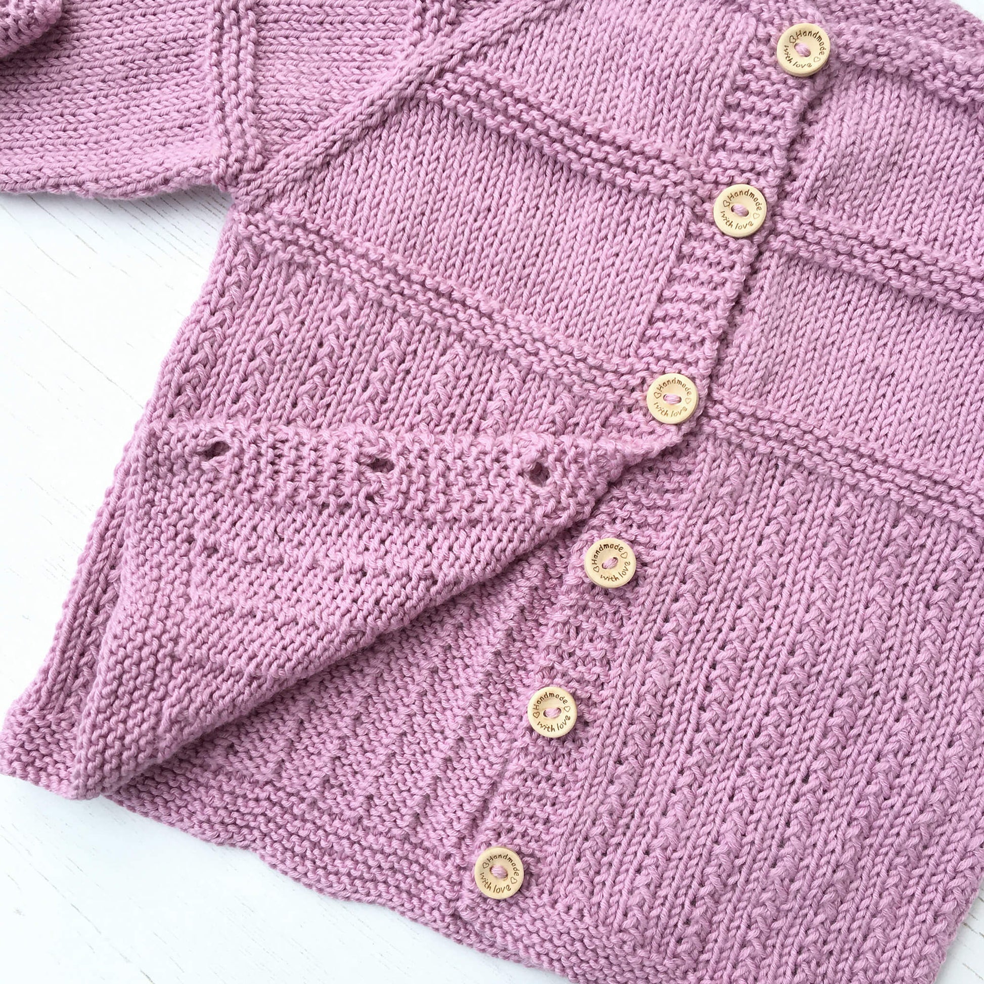 a knit pattern for a baby cardigan. the lower buttons are open showing the inside of the cardigan