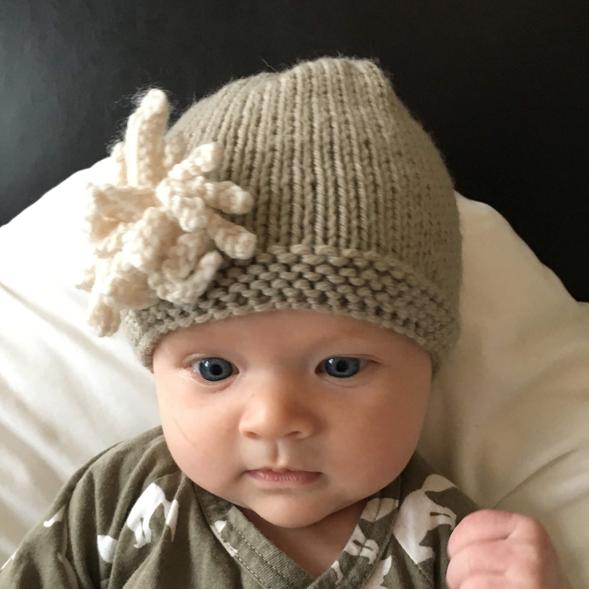 a knitting pattern for a baby hat with a flower modelled by a baby