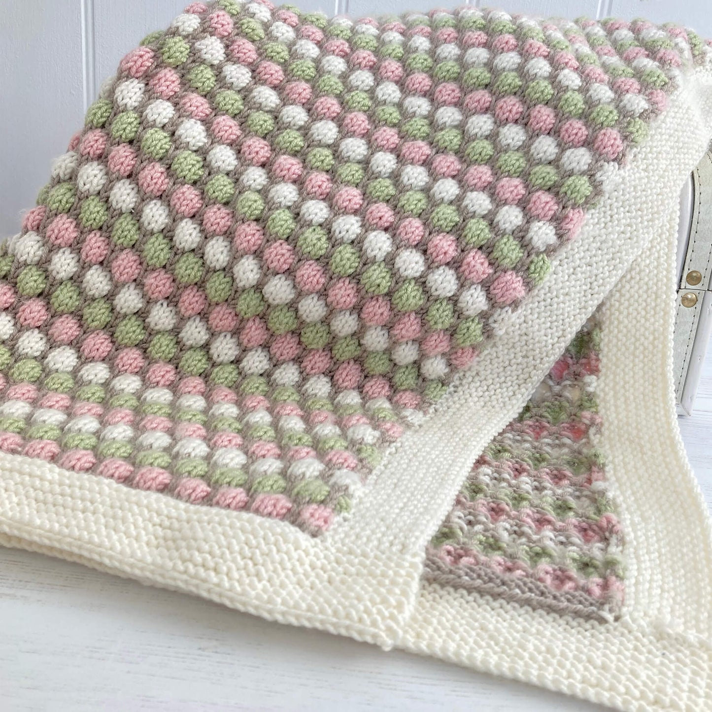 knitting pattern for a baby blanket . sample is shown draped over a toy chest