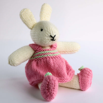 a knitting pattern for bunnies. the girl bunny shown is sitting wearing a bright pink dress