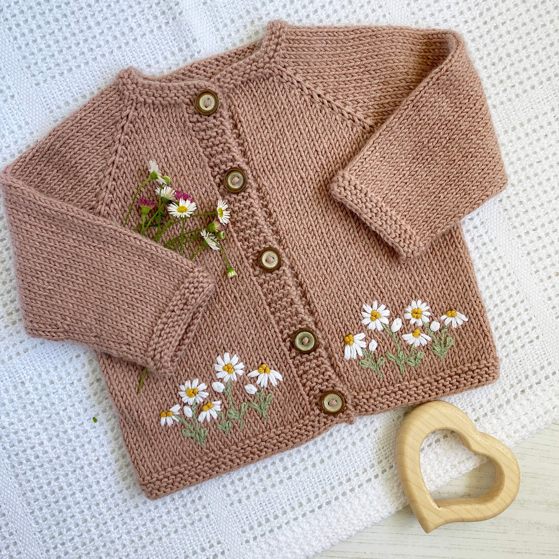 a baby cardigan knitting pattern with daisy embroidery along the bottom front edge