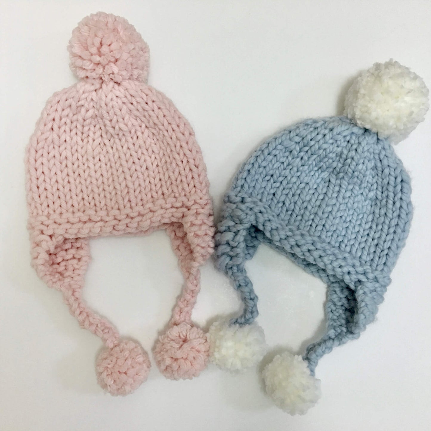 a knitting pattern for a simple hat with pompoms. samples are shown in pale pink and pale blue