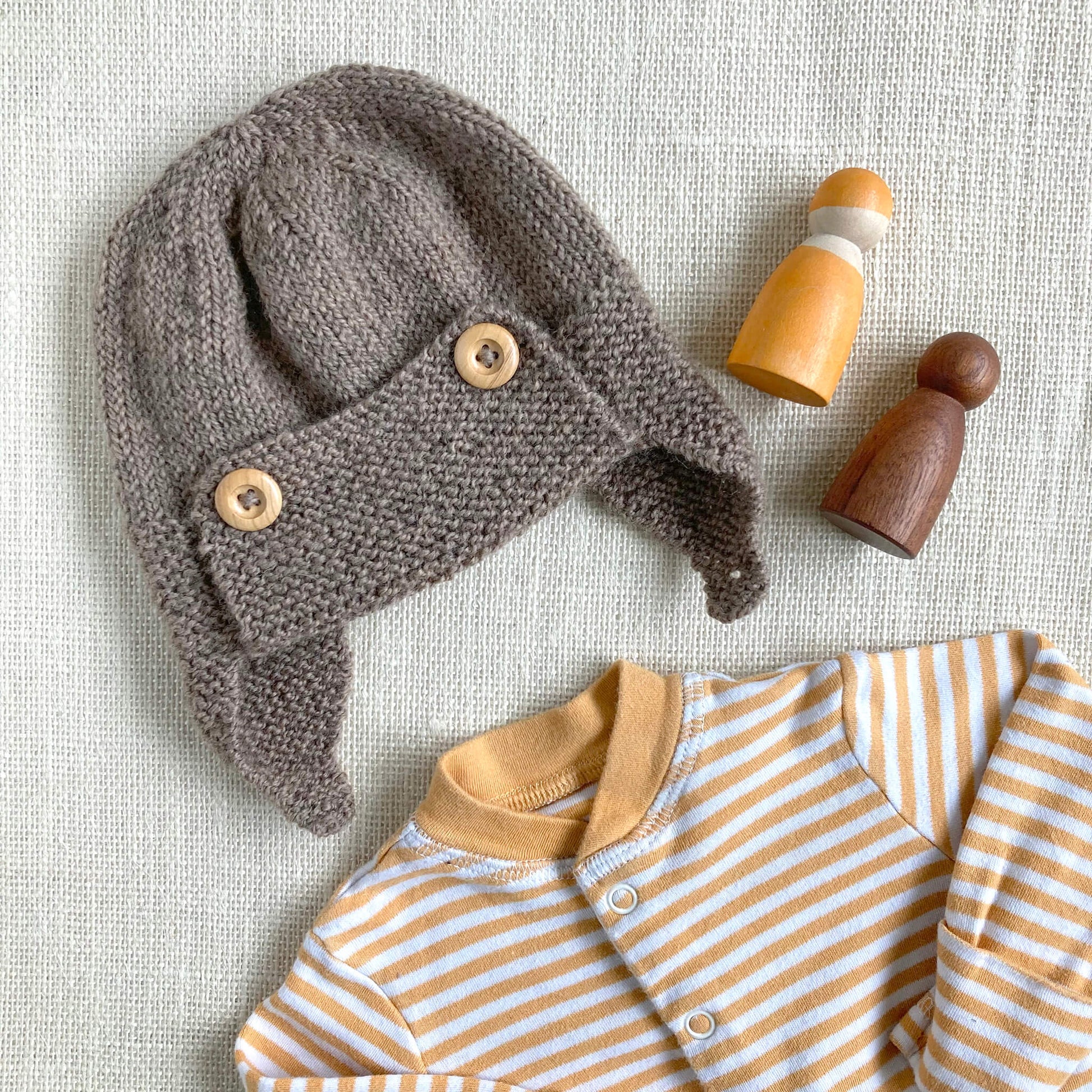 a flat lay showing a pilot hat knitting pattern for a baby paired with a sleepsuit and toys