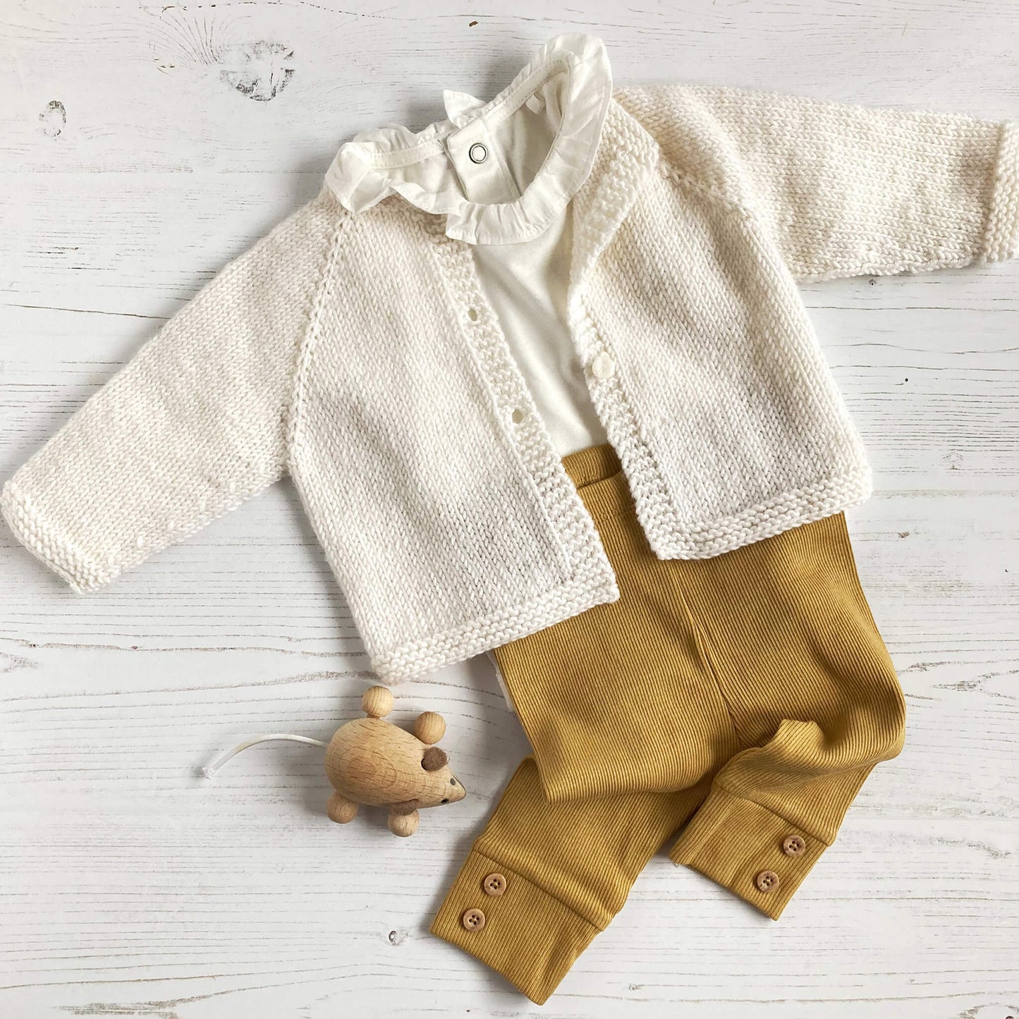 a simple baby cardigan knitting pattern styled with mustard leggings and small toy