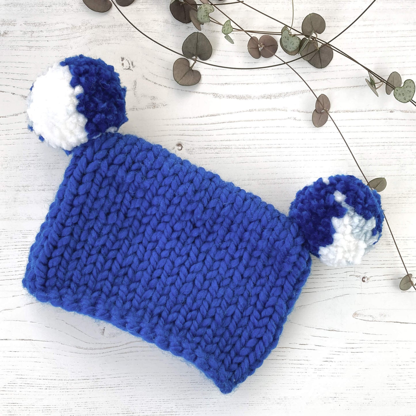 a simple beginner baby hat knitting pattern for a square hat with pompoms