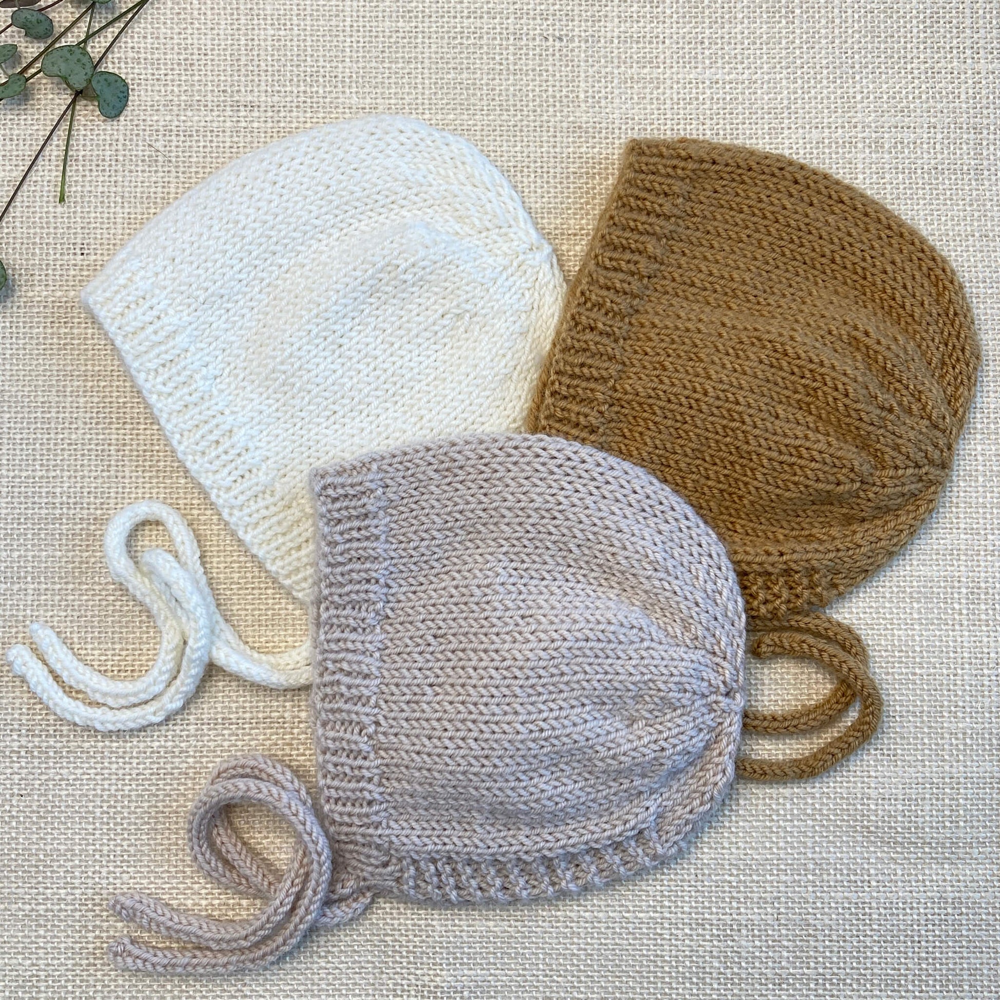 a simple bonnet knitting pattern. 3 samples are shown, knit in grey, white and mustard colour yarn